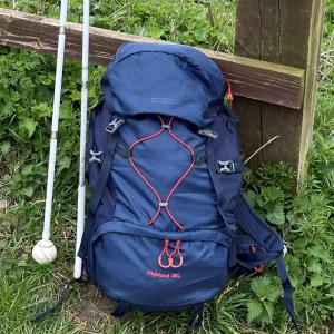 A blue backpack leaning against a fence with two white canes beside it