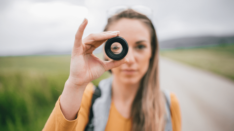 A blurred image of a woman holding up a lens to their eye which is seen in clear view