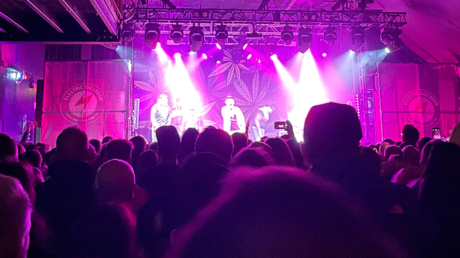 A band on a stage in front of a crowd with their arms in the air