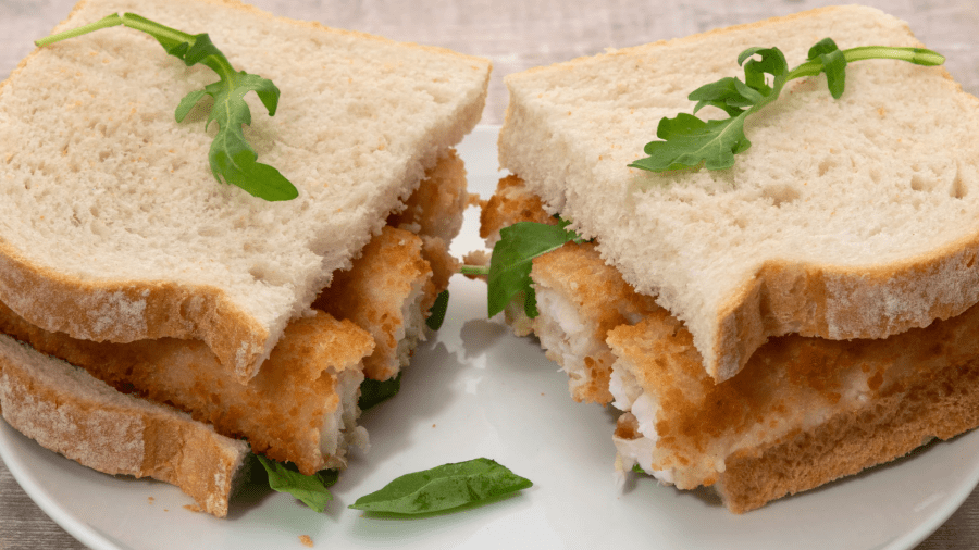 A fish finger sandwich on soft white bread artistically arranged on a plate